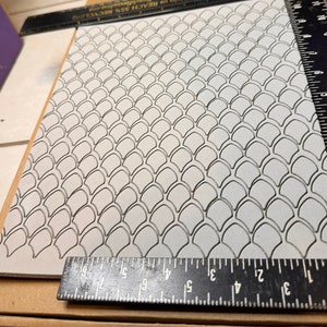 Op de afbeelding: Een witte rubberen stempel met een herhalend patroon van zwarte omlijnde schubben. De stempel is ongeveer 15 cm bij 10 cm.