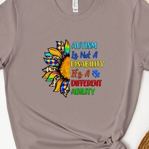 May include: A gray t-shirt with a colorful sunflower design and the text "AUTISM Is Not A DISABILITY It's A DIFFERENT ABILITY".
