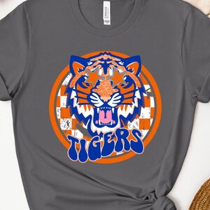 May include: A gray t-shirt with a retro orange and blue tiger graphic. The tiger has blue sunglasses and the text "TIGERS" is in a retro font.