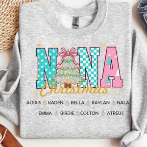May include: A light gray sweatshirt with the word "NANA" in teal and pink letters, with a Christmas tree graphic. The word "Christmas" is in gold script below. Names of family members are listed below the text.