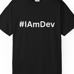 Puede incluir: Una camiseta negra de manga corta con el texto blanco #IAmDev impreso en el centro del pecho. La prenda tiene un cuello redondo y un corte estándar, con una pequeña etiqueta de marca blanca visible en el interior de la zona del cuello.