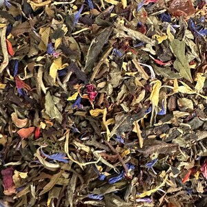 May include: A close-up of a blend of white tea, dried fruit, and flower petals. The tea blend is a mix of white tea leaves, dried fruit pieces, and flower petals in shades of red, yellow, and blue.