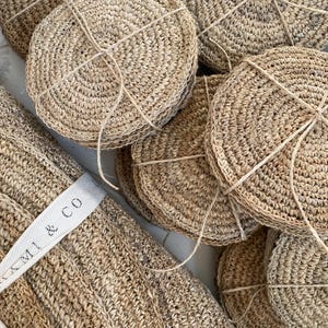 May include: A stack of round, natural fibre coasters with a label that reads "ML & CO". The coasters are made of a woven material and are tied together with twine.