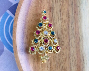May include: A gold-tone Christmas tree brooch with red, green, and clear rhinestones.