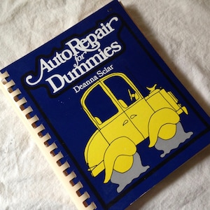 May include: A spiral-bound book titled "Auto Repair for Dummies" with a blue cover. The cover features a yellow cartoon car with gray water or mud around the tires. The title is in white script, and the author's name is also visible.