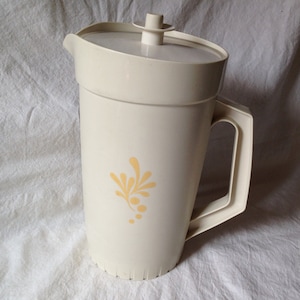 May include: A white plastic pitcher with a yellow floral design. The pitcher has a lid and a handle.