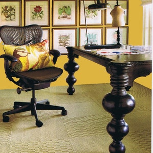 May include: A black office chair with a woven back and a yellow pillow sits in front of a desk with a dark wood top and legs. The desk is against a yellow wall with framed botanical prints.