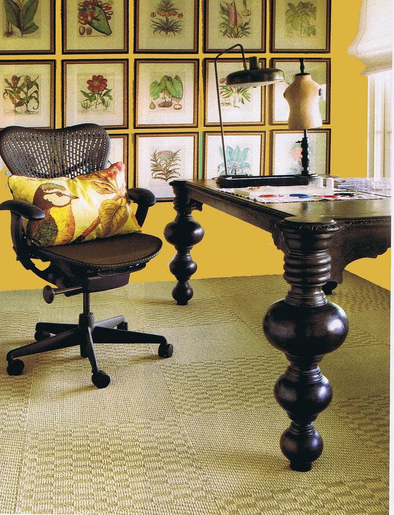 May include: A black office chair with a woven back and a yellow pillow sits in front of a desk with a dark wood top and legs. The desk is against a yellow wall with framed botanical prints.