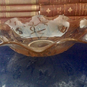 May include: A clear glass bowl with a wavy rim and a decorative pattern on the bottom. The bowl is sitting on a blue surface.