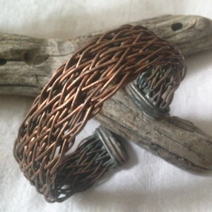 May include: A woven copper bracelet with a braided design. The bracelet is made of multiple strands of copper wire that are woven together to create a textured and intricate pattern.