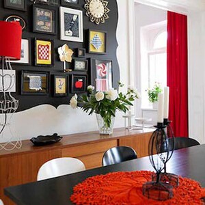 May include: A black dining table with a red crocheted table runner and a black metal candle holder with white candles. The table is set with white chairs and a wooden sideboard with a black and white patterned wall behind it.