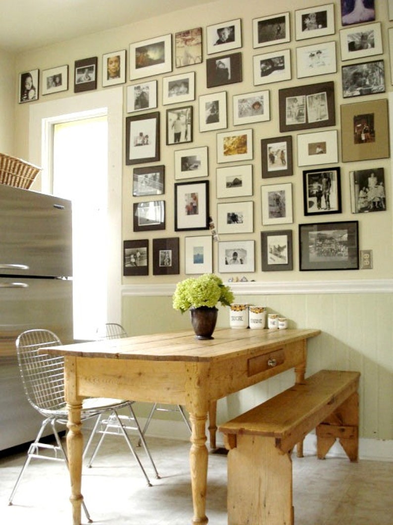 May include: A light wood dining table with a single drawer and a matching bench. The table has turned legs and is set against a wall covered in framed black and white photos.