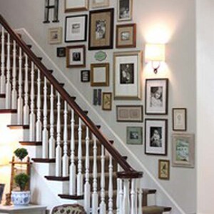 May include: A white staircase with a wooden handrail and a wall decorated with a gallery of framed pictures in various sizes and styles. The pictures include black and white photos, landscapes, and abstract art.