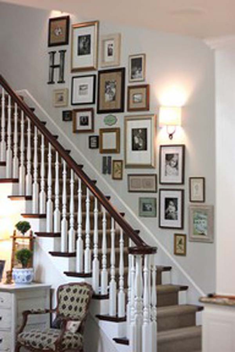 May include: A white staircase with a wooden handrail and a wall decorated with a gallery of framed pictures in various sizes and styles. The pictures include black and white photos, landscapes, and abstract art.