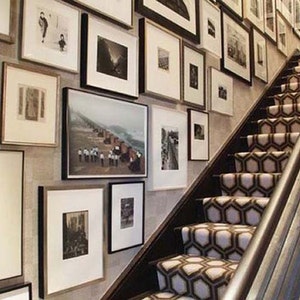 Peut inclure: Un escalier avec un tapis d'escalier &agrave; motifs dans des tons de brun et de blanc. Les murs sont d&eacute;cor&eacute;s d'une galerie de photographies et d'&oelig;uvres d'art en noir et blanc encadr&eacute;es.