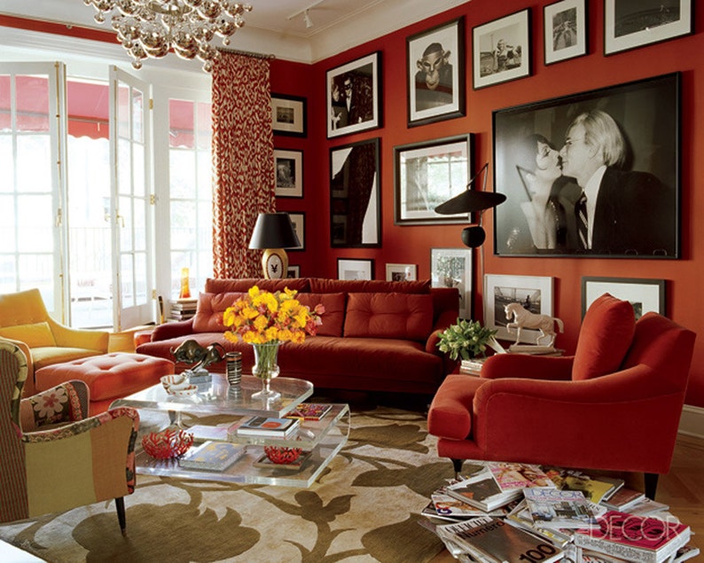 May include: A living room with red walls and a red velvet sofa, two red armchairs, a glass coffee table, and a yellow floral arrangement. The room is decorated with framed black and white photographs.