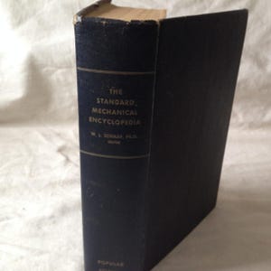 May include: A black book with gold lettering on the spine. The title is "The Standard Mechanical Encyclopedia" with the author listed as "W.L. Schaaf, Ph.D. Editor".