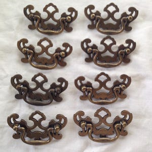 May include: Eight antique brass drawer pulls with a decorative, ornate design. Each pull has a loop handle and a decorative, intricate design.