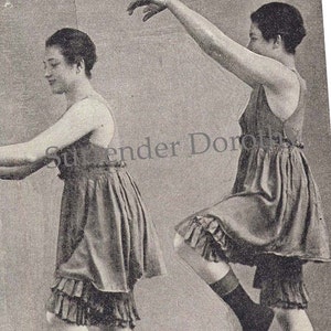 Puede incluir: Dos mujeres con vestidos sin mangas y dobladillos con volantes. Los vestidos son de color gris oscuro y las mujeres están de pie en un estudio.