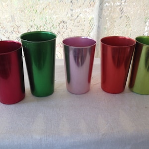 May include: Five metal drinking cups in different colors: red, green, pink, red, and green. The cups are lined up in a row on a white surface.
