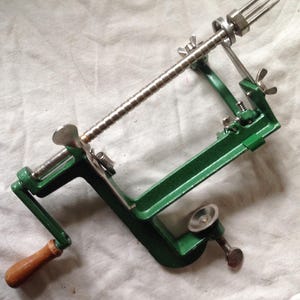 May include: Green metal apple peeler with a wooden handle and a stainless steel blade. The peeler has a crank to turn the blade.