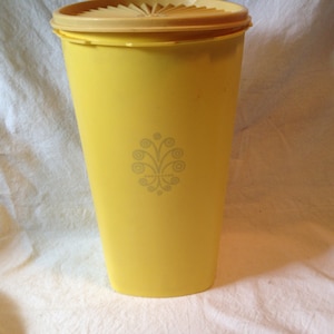 May include: A yellow plastic container with a beige lid and a decorative design. The container is tall and cylindrical.