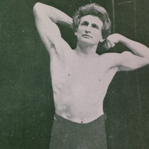 May include: A black and white photo of a man with his arms raised above his head, flexing his biceps. He is wearing black shorts.