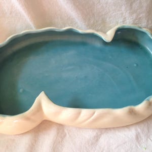 May include: A white ceramic dish with a blue glaze inside. The dish has a wavy, organic shape.