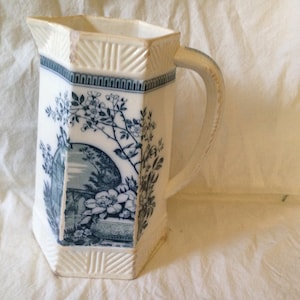 May include: A white ceramic pitcher with a blue and white floral design. The pitcher has a hexagonal shape and a handle.