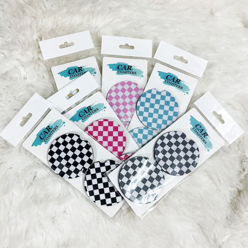 May include: Set of six car coasters featuring a checkered pattern in black and white, pink and white, and blue and white. The coasters are packaged in individual clear plastic sleeves with the words "Car Coasters" printed on each sleeve.