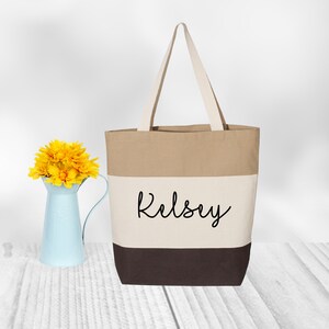 May include: A beige, white, and brown canvas tote bag with the name "Kelsey" printed in black on the front.