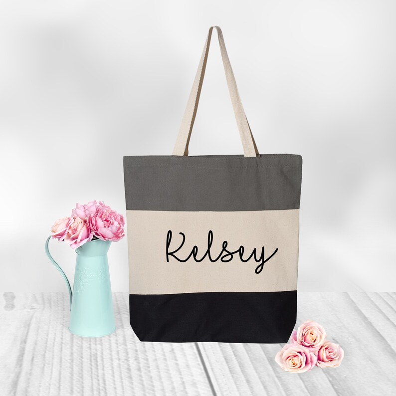 May include: A gray, beige, and black striped canvas tote bag with the name "Kelsey" written in black cursive on the beige stripe.