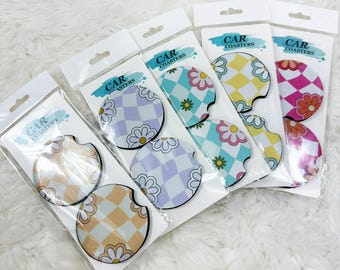 May include: Set of six car coasters with a checkered and daisy pattern. The coasters come in four different color combinations: pink and white, yellow and white, blue and white, and purple and white. Each set includes the text "CAR COASTERS".
