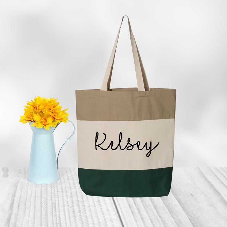 May include: A beige, white, and green canvas tote bag with the name "Kelsey" printed in black cursive on the front.