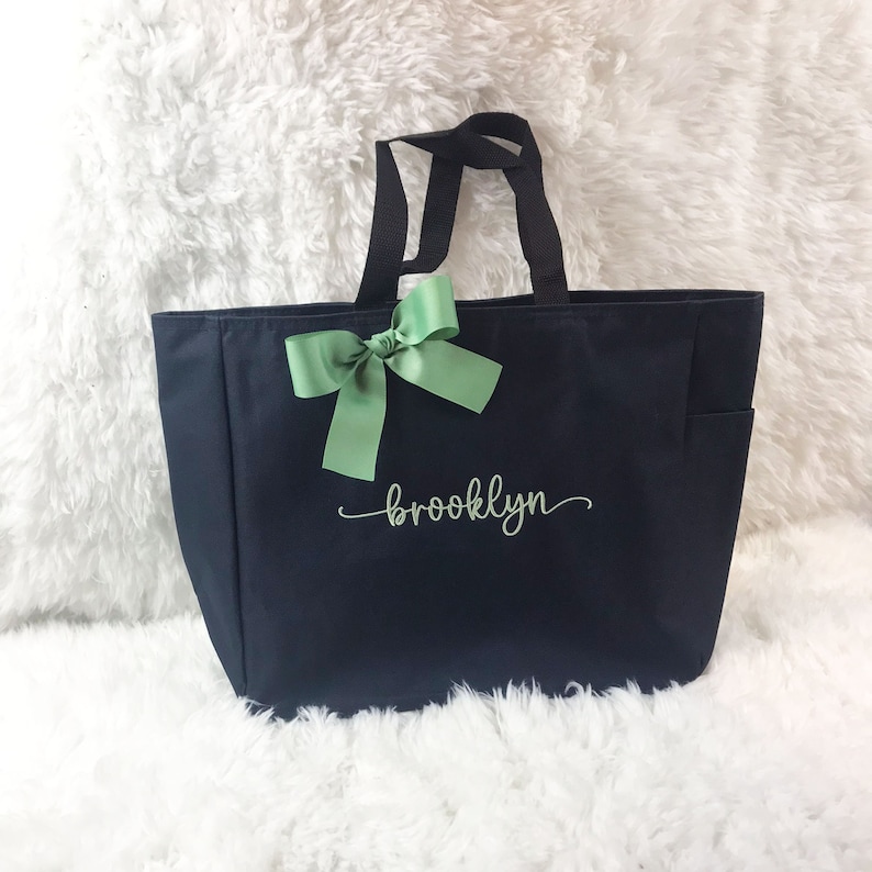 May include: Black canvas tote bag with a green bow and the name "brooklyn" embroidered in green cursive.