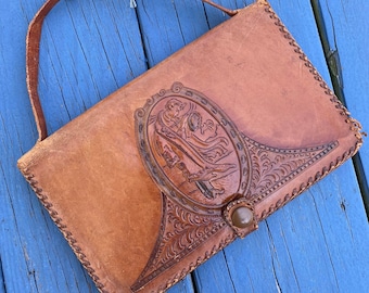 May include: A brown leather purse with a tooled design featuring a woman in a long dress. The purse has a flap closure with a button and a short strap.