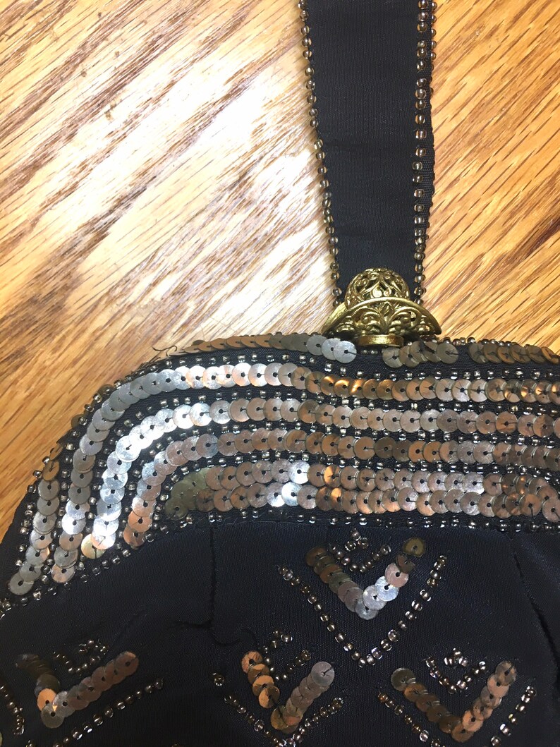May include: A black beaded evening bag with a gold clasp and a gold and silver sequined design.