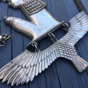 May include: Silver pendant featuring a hand with a detailed design and a pair of wings. The wings are made of a textured metal and have a detailed feather design.