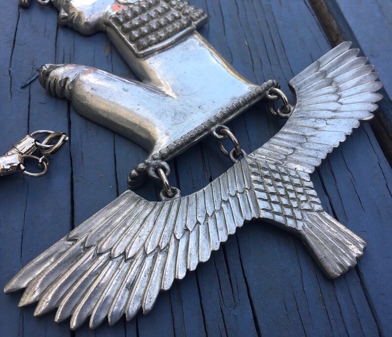 May include: Silver pendant featuring a hand with a detailed design and a pair of wings. The wings are made of a textured metal and have a detailed feather design.