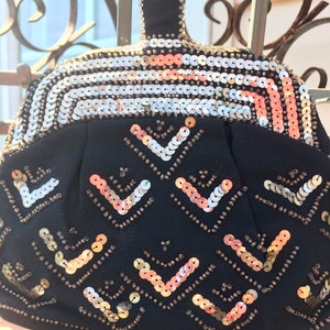 May include: A black evening bag with a gold and silver sequined design. The bag has a top handle and a geometric pattern of sequins.