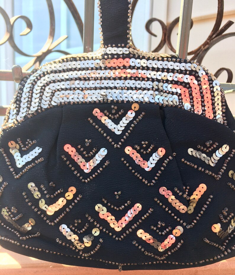 May include: A black evening bag with a gold and silver sequined design. The bag has a top handle and a geometric pattern of sequins.