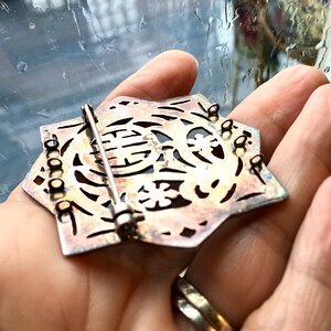 May include: A silver-toned, star-shaped brooch with intricate cut-out designs. The brooch has a pin and catch closure on the back.