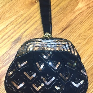 May include: A black evening bag with a gold and silver sequined design. The bag has a black fabric handle.