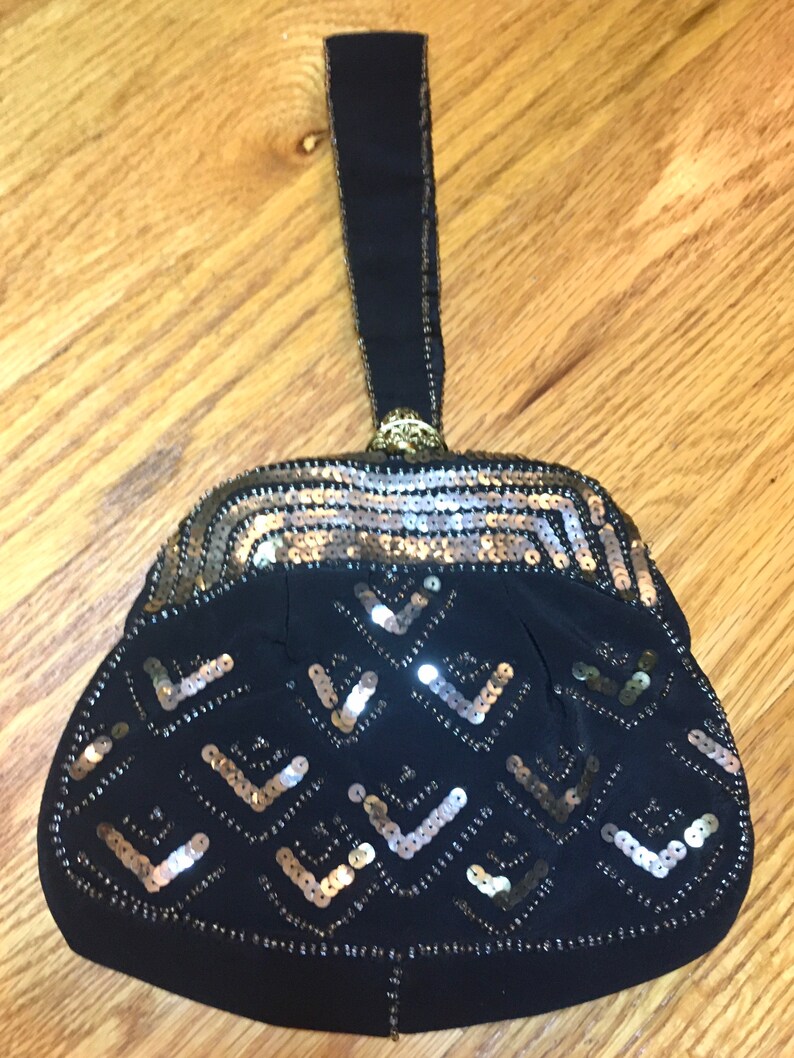 May include: A black evening bag with a gold and silver sequined design. The bag has a black fabric handle.