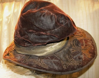 May include: A brown velvet hat with a wide brim and gold trim. The brim is decorated with a braided design.