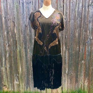May include: A vintage 1920s flapper dress with a black velvet skirt and a green silk bodice. The bodice is adorned with gold embroidery and a floral design. The skirt has a fringe trim.