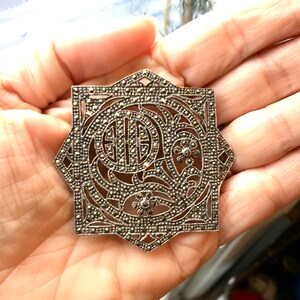 May include: A silver and marcasite brooch with a geometric design and a floral motif. The brooch is in the shape of a star and has a filigree design.