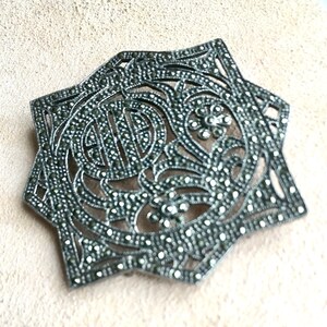 May include: A silver brooch with a star-shaped design, set with marcasite stones. The brooch is intricate and detailed, with a floral motif.