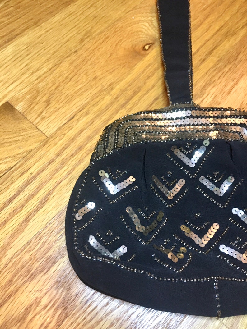May include: A black evening bag with a gold and silver sequined design. The bag has a single strap and a rounded shape.