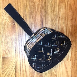 May include: A black evening bag with a gold and silver sequined design. The bag has a long black strap.